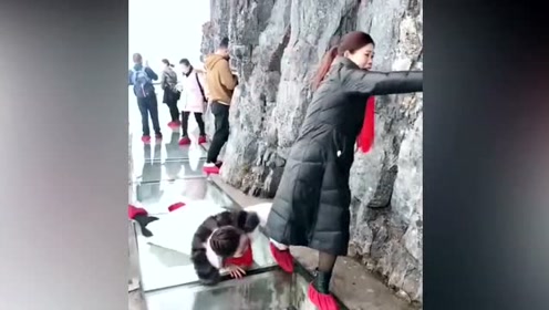 女子在玻璃栈道上爬行,突然抓住另一女子的脚,女子被她抓倒了!