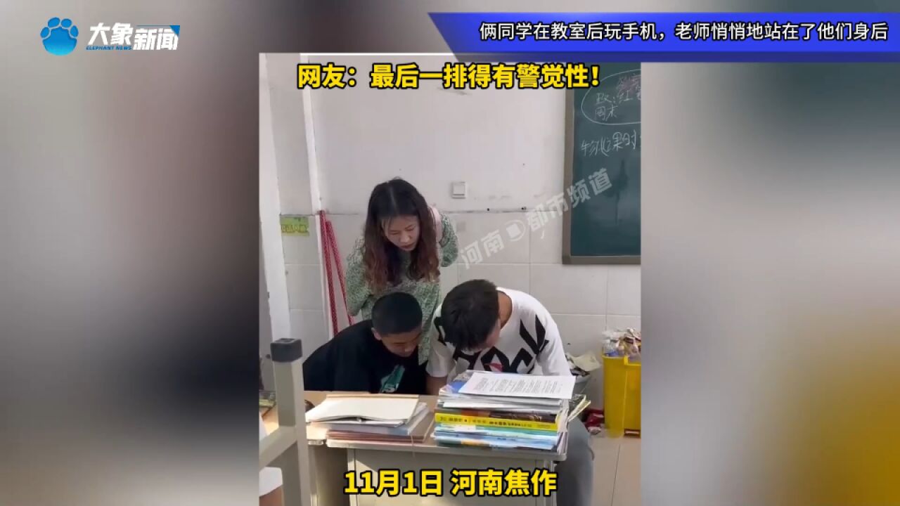 俩同学在教室后玩手机,老师悄悄地站在了他们身后