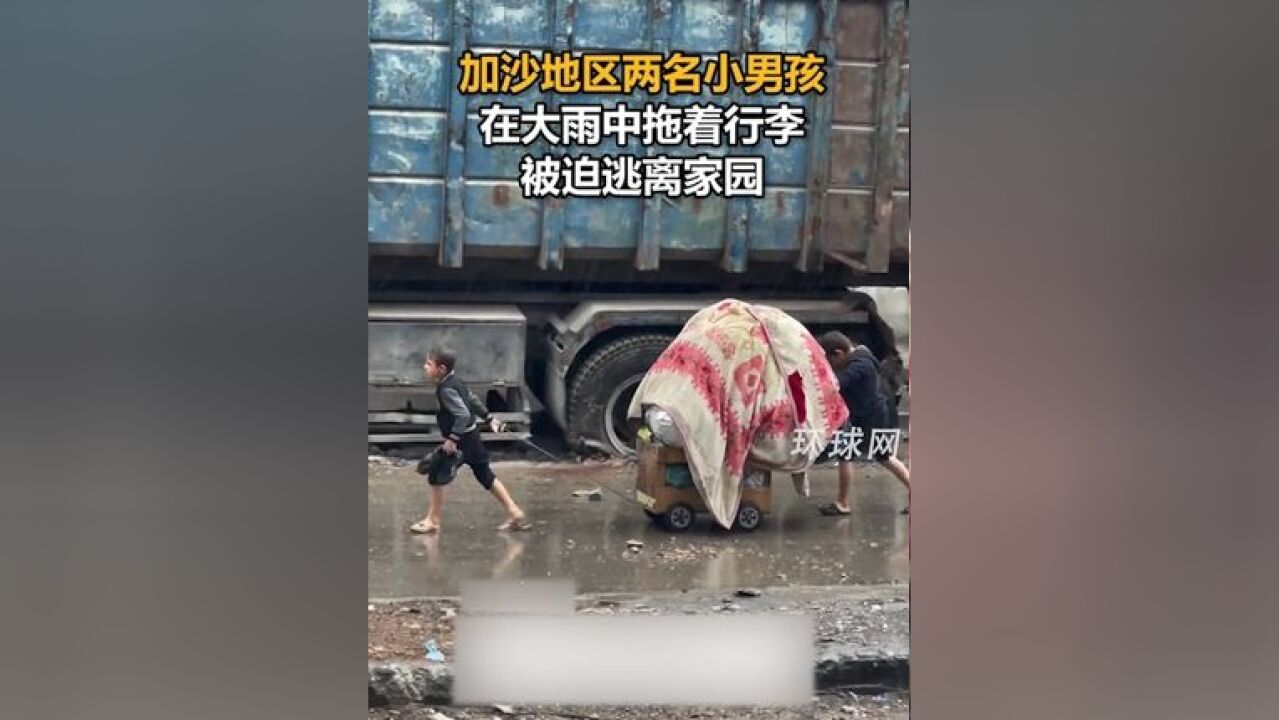 加沙地区两名小男孩在大雨中拖着行李,被迫逃离家园