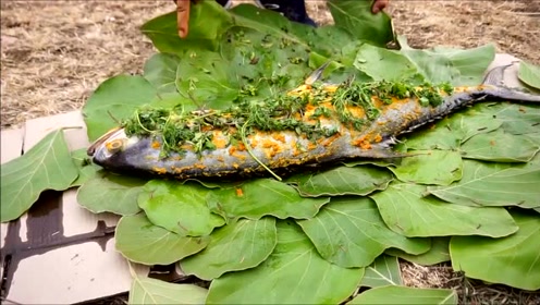 小伙抹上调料用树叶包起来鱼,烤着吃