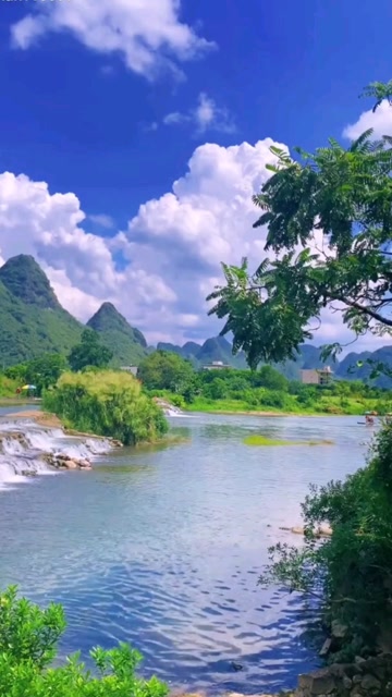 河流在蓝天白云下潺潺流水清澈见底,远处青山耸立!