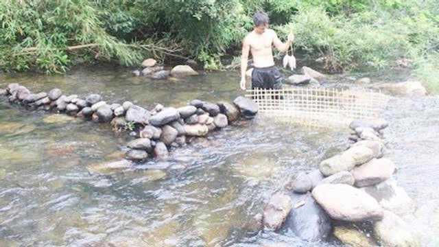 小伙在河道建造一座石坝,手工制作渔网,原地烤鱼吃的真开心