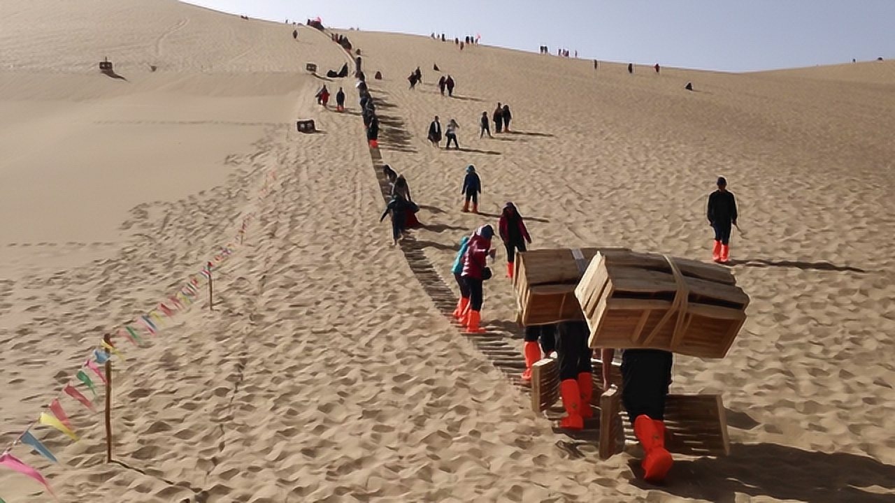 負重前行鳴沙山背滑沙板上山的人