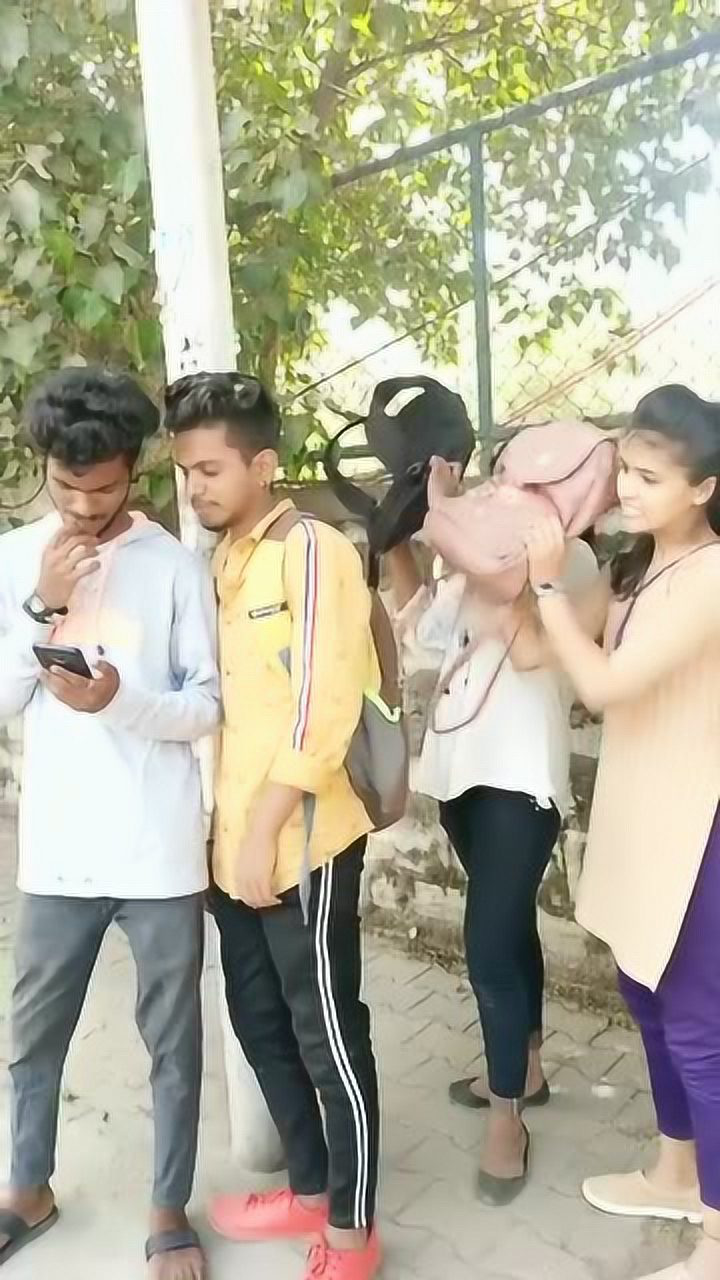 两个印度小哥玩手机,后面女朋友看到了拿书包打