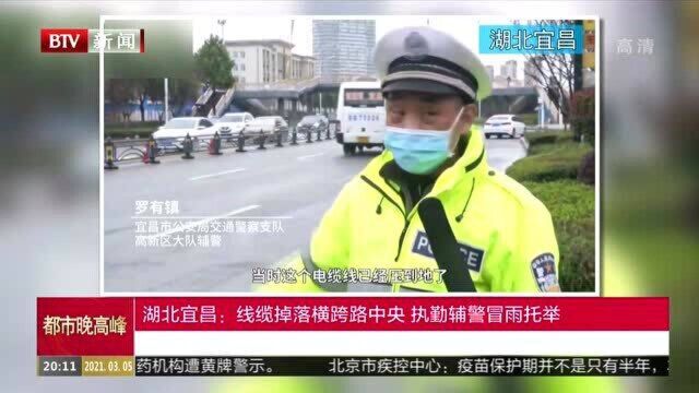 湖北宜昌:线缆掉落横跨路中央 执勤辅警冒雨托举